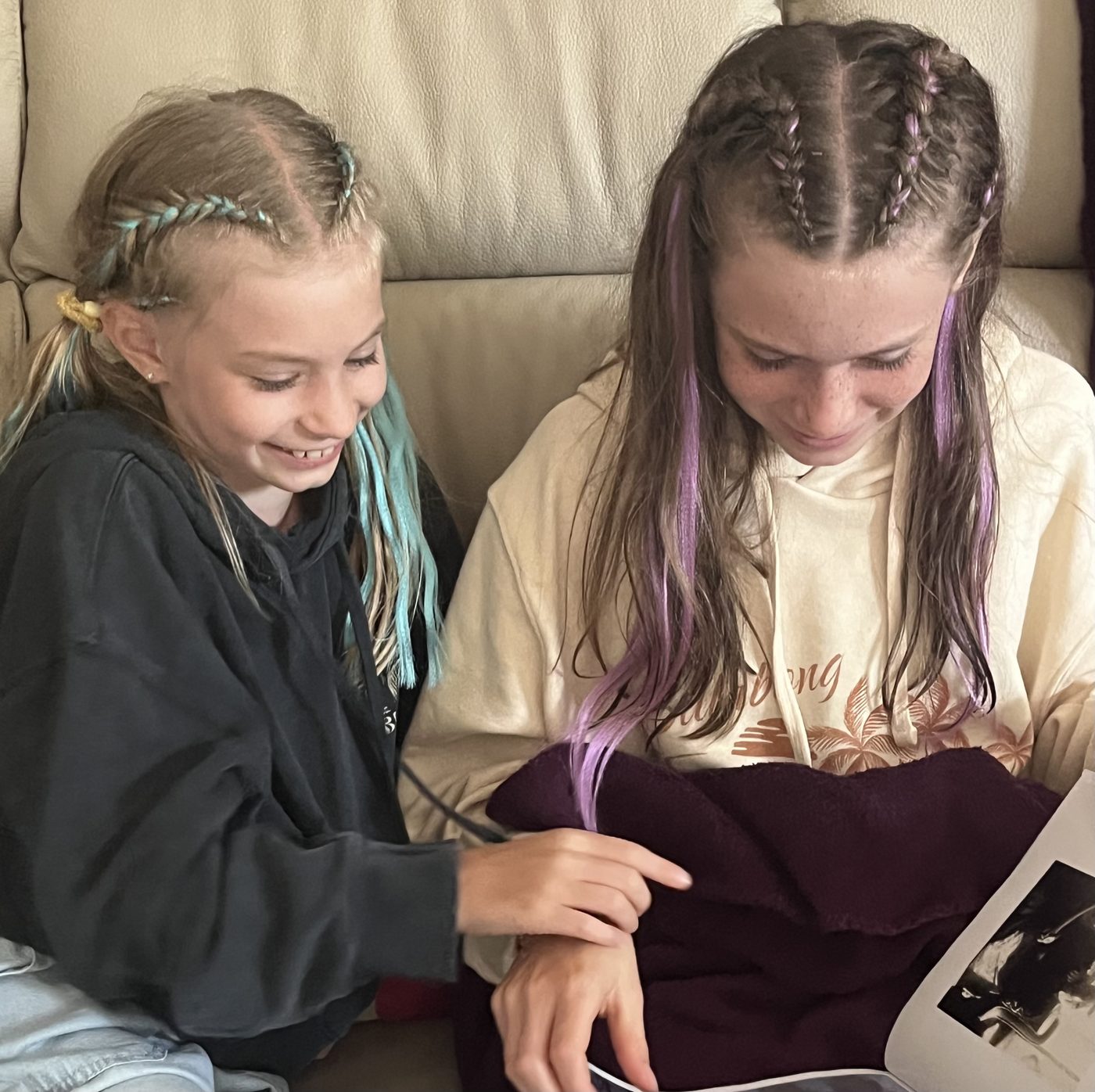 Deux jeunes filles complices regardent ensemble un album photo, souriantes.